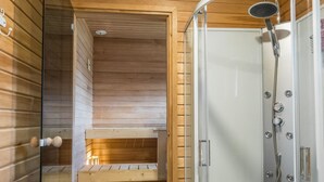 Interior de una cabaña de madera con sauna, zona de ducha y un banco.