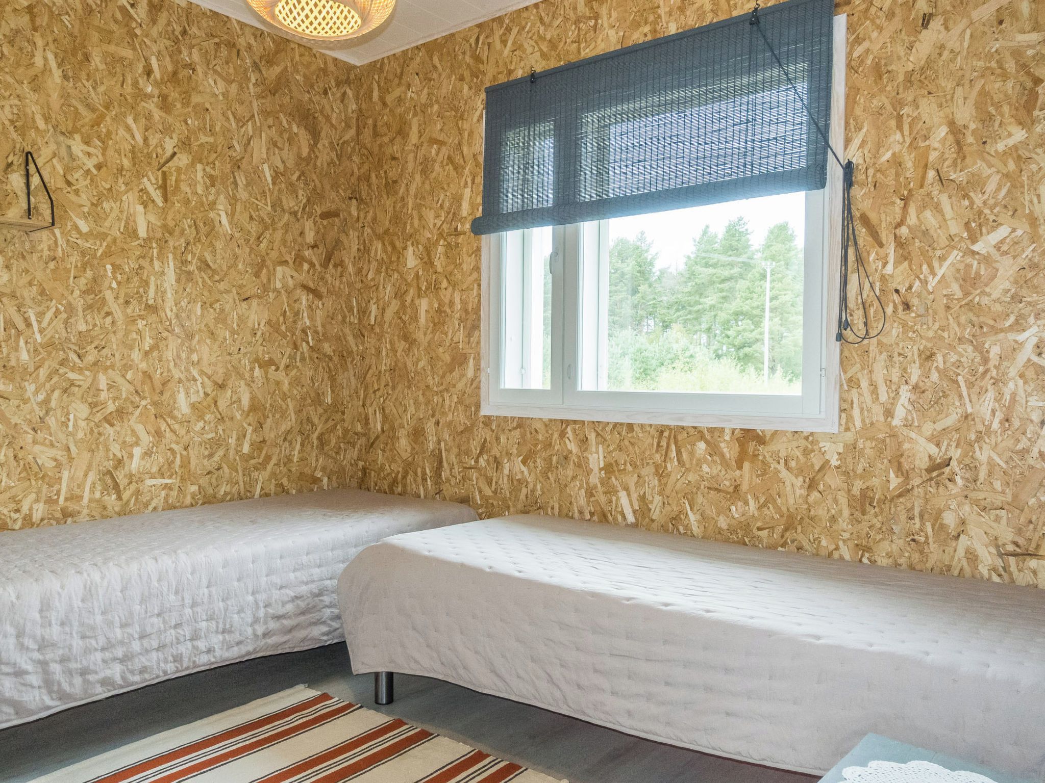 Une chambre avec deux lits simples, une fenêtre donnant sur la verdure et un mur en bois.