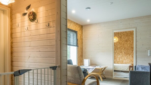 Habitación acogedora con cama, una silla y una mesita. Pared de madera con ganchos y un adorno.
