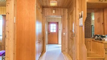 Un couloir en bois, avec une porte au bout, une fenêtre donnant sur un paysage et un luminaire au plafond.