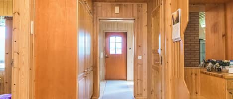 A wooden hallway with a door at the end, a window with a view, and a light fixture on the ceiling.