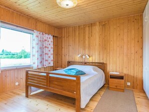Een kamer met houten lambrisering, een bed, nachtkastje en een raam met gordijnen.