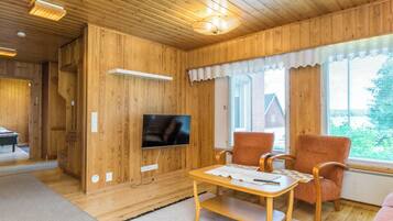 A wooden-paneled room with a television, a table, two chairs, and a sofa.