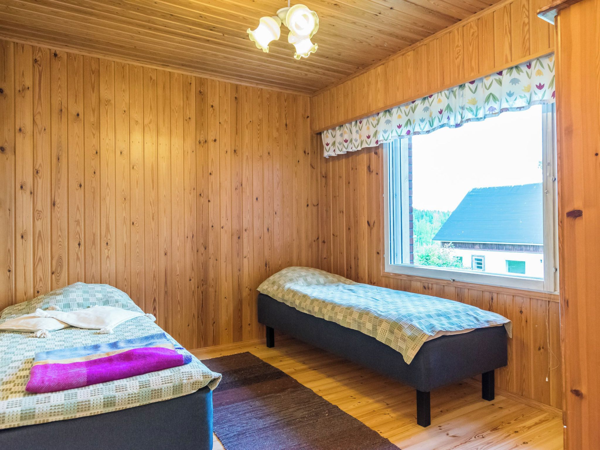 A room with wooden walls and a window with a patterned curtain. There are two beds with different bedding.