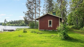 A small red cabin with a dock extending into a lake, surrounded by dense forest.