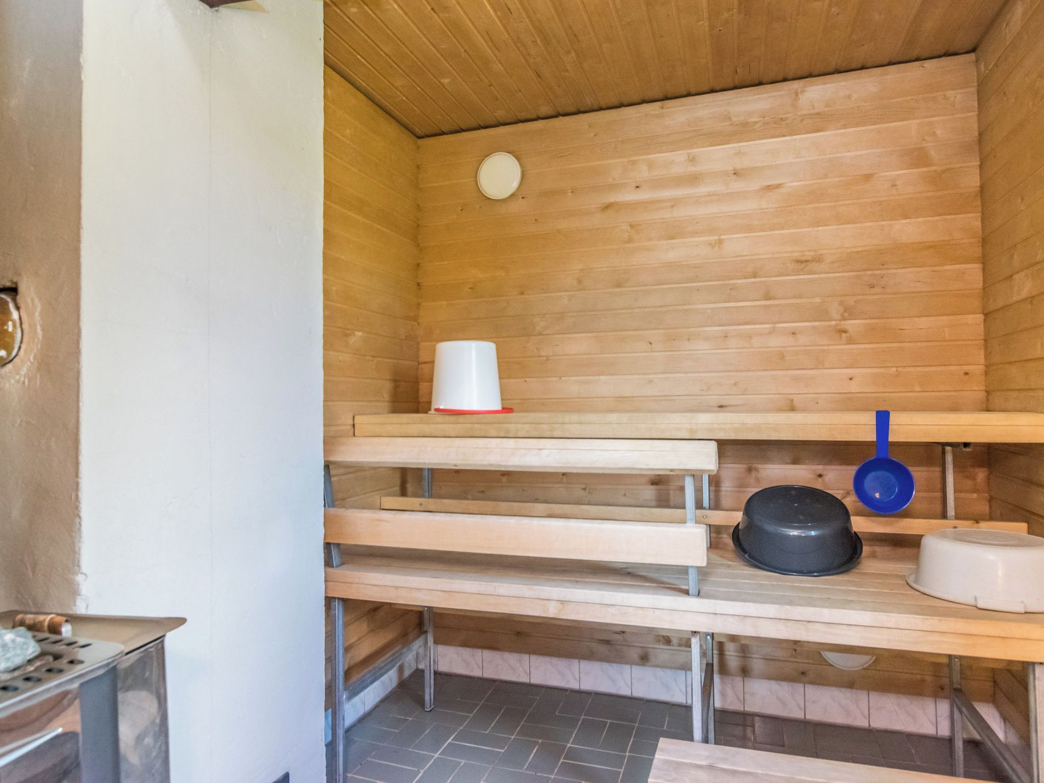 Un sauna con bancos de madera, un recipiente blanco, una olla negra y una cuchara de servir azul.