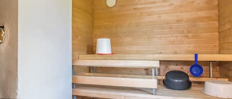A sauna room with wooden benches, a white basin, a black pot, and a blue ladle.