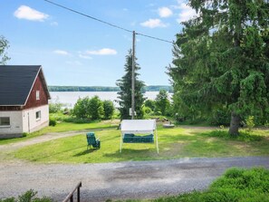 A rustic cabin with a gravel path leading to a covered seating area, overlooking a lake.
