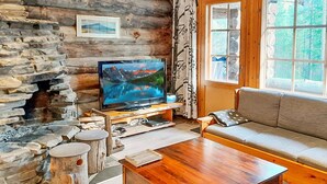 A cozy living room with a stone fireplace, a television, a wooden coffee table, and a sofa. - Vacation home Rakka by Interhome (Kittilä)
