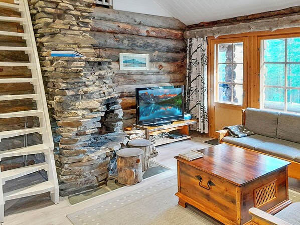 A cozy cabin interior with a stone wall, a television, a wooden coffee table, and a sofa.