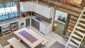 A modern kitchen with a built-in washing machine, a dining area with a table and benches, and a staircase leading to an upper level. - Vacation home Rakka by Interhome (Kittilä)