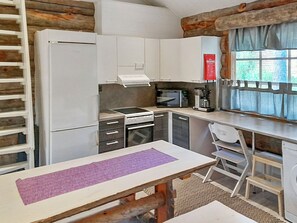 A compact kitchen with a refrigerator, microwave, stove, and coffee maker. There's a window with curtains and a fire blanket on the wall.