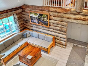 A log cabin interior with a sectional sofa, wooden coffee table, and a framed cityscape painting.