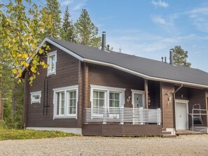 A wooden cabin with a porch, a chimney, and a gravel driveway.