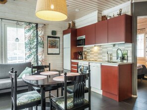 Cocina compacta con gabinetes rojos, comedor con mesa y sillas redondas, y lámpara colgante.