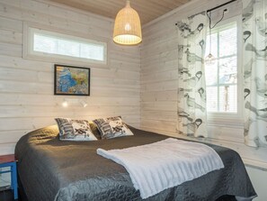 A bedroom with a large bed, two pillows, a hanging light fixture, a painting on the wall, and a window with curtains.