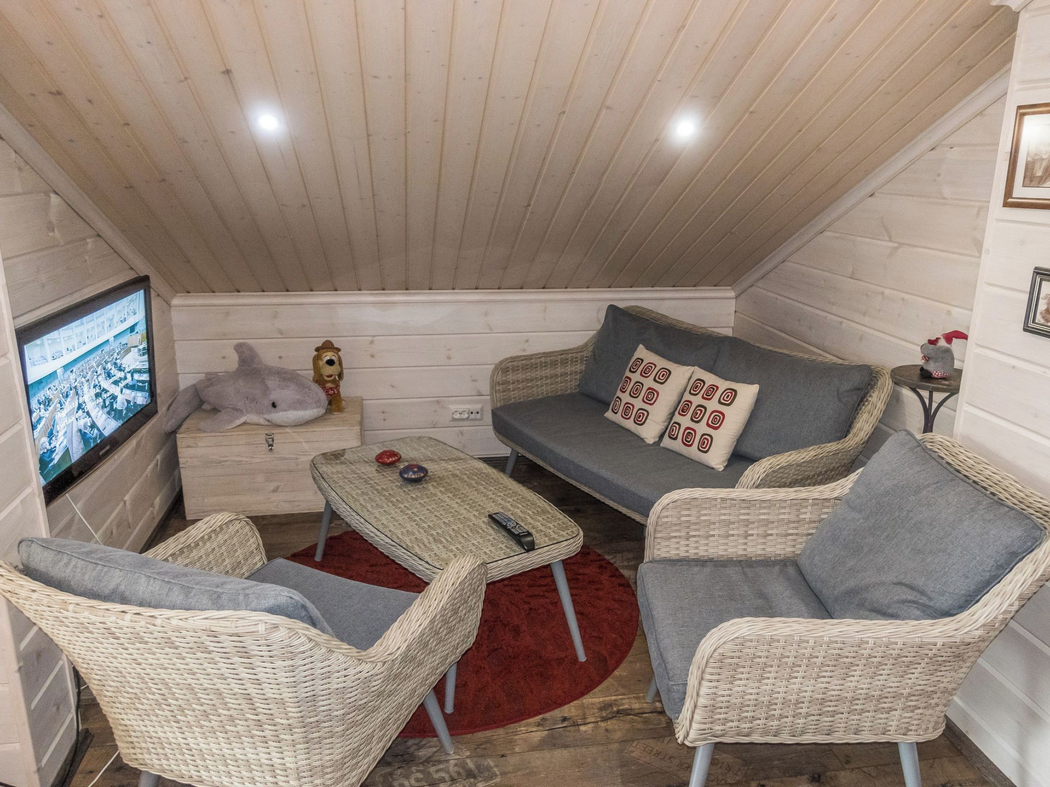 Ein gemütliches Zimmer mit Fernseher, Korbmöbeln und einem roten Teppich.