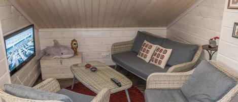 Ein gemütliches Zimmer mit Fernseher, Korbmöbeln und einem roten Teppich.