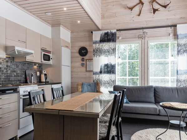 A modern kitchen with a dining area, featuring a large window with blinds, a sofa, and a decorative wall piece.