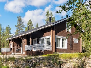 En træhytte med veranda, store vinduer og skorsten.
