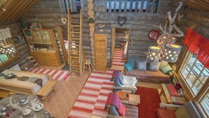 Interior acogedor de una cabaña de madera con cama en altillo, chimenea y mesa de comedor rústica de madera.