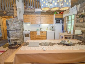 A rustic cabin interior with a stone fireplace, wooden cabinets, a kitchenette, and a bed with a floral bedspread.