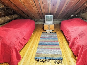 Une petite chambre accueillante avec deux lits simples, un plancher en bois et un téléviseur posé sur un meuble en bois.
