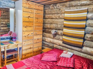 A log cabin room with a wooden wardrobe, a bed with red bedding, and a striped wall hanging. - Saaruatar by Interhome (Kuusamo)