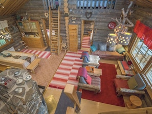 A cozy log cabin interior with a loft bed, wooden furniture, and a fireplace.
