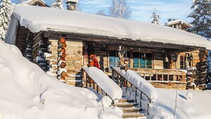 Una cabaña de troncos con una escalera de madera que lleva a un porche, rodeada de nieve.