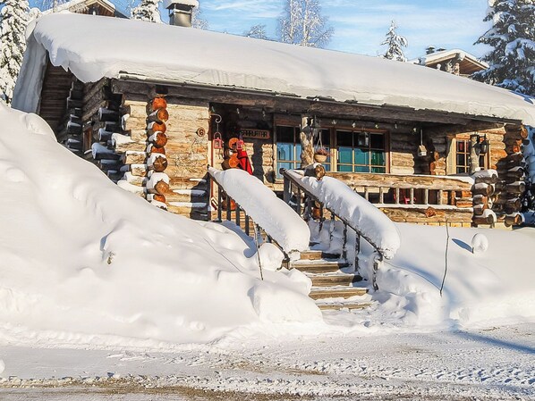 Une cabane en rondins avec un escalier en bois menant à une véranda, le tout entouré de neige.