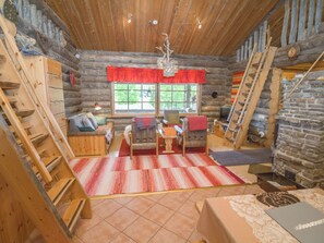 A log cabin interior with a wooden staircase, a fireplace, a dining area, and a window with a view of greenery. - Saaruatar by Interhome (Kuusamo)