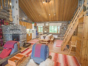 Ein rustikales Blockhaus im Inneren mit Kamin aus Stein, Holzwänden, einem Essbereich und einer Treppe.