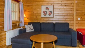 Acogedora habitación tipo cabaña de madera con un sofá gris oscuro, una mesita pequeña y un radiador.