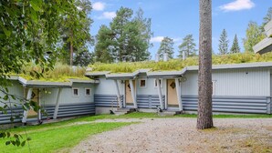 Una hilera de cabañas de madera con un sendero de grava al frente, rodeadas de árboles y un cielo despejado.