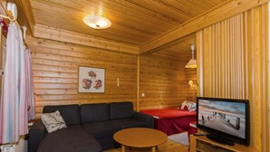 Una cabaña acogedora con interior de madera, un sofá, una pequeña mesa, un televisor y una cama.