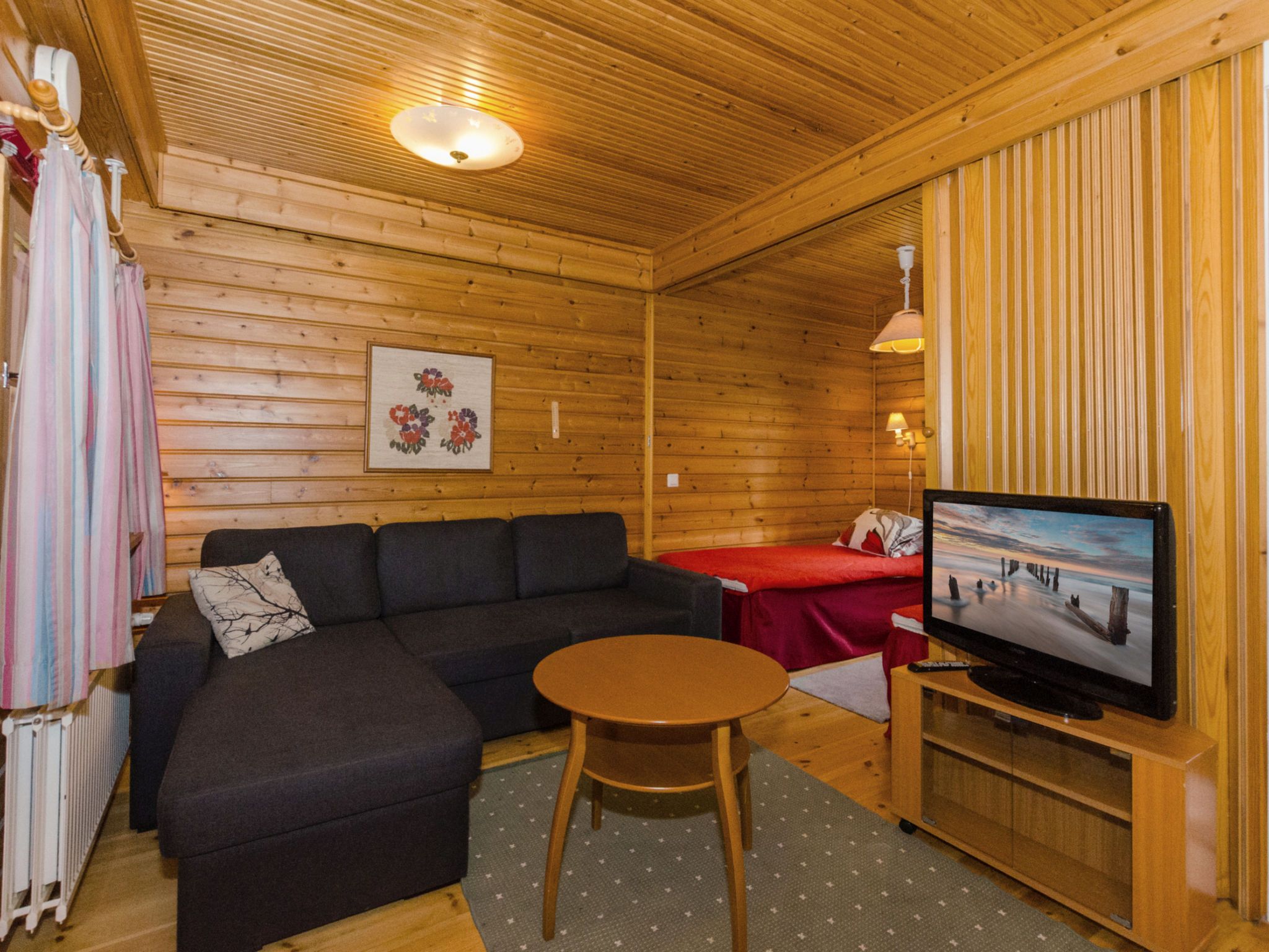 Kodikas huone, jossa on sohva, pieni pöytä, televisio ja sänky.