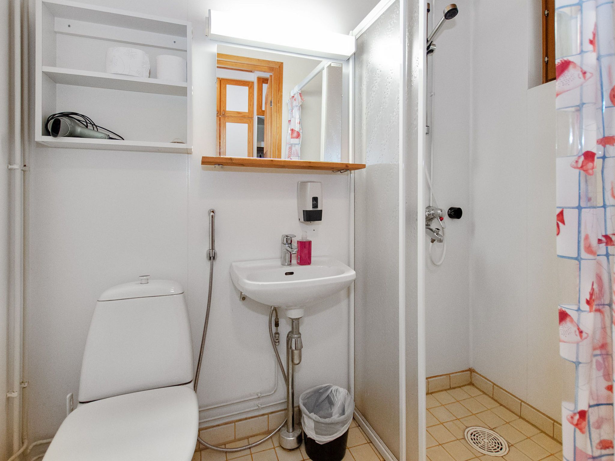 A bathroom with a toilet, sink, shower, and a small shelf with toiletries.