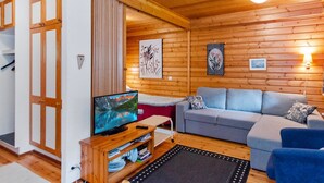 A cozy cabin interior with a wooden ceiling, a television on a wooden stand, a grey sofa, and a blue armchair.