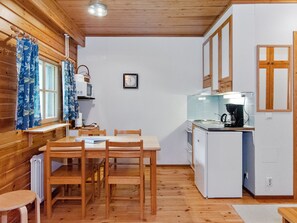 A compact kitchen with wooden walls, a dining table with chairs, a microwave, a refrigerator, and a coffee maker.