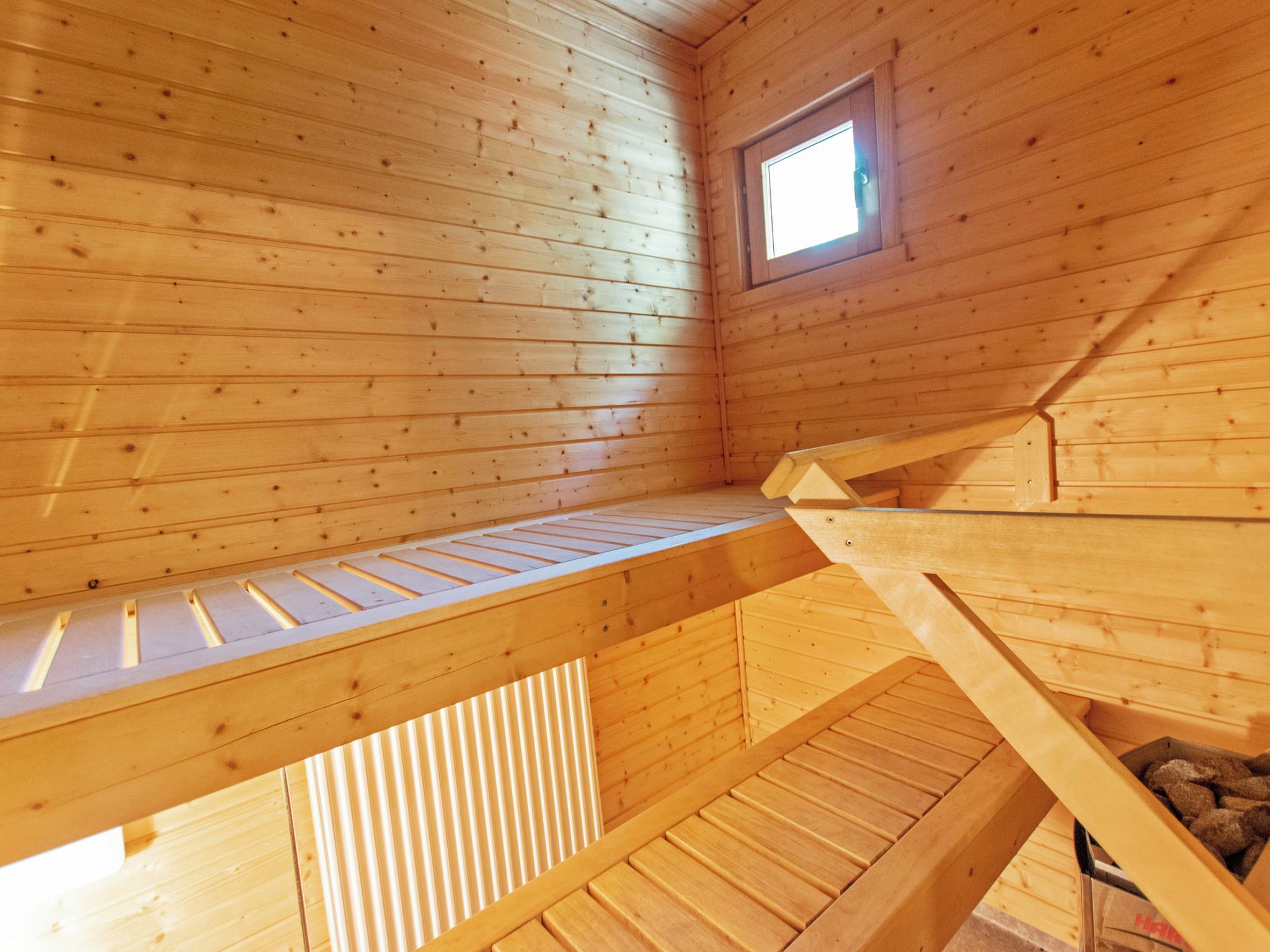 Ein Holzblock-Innenraum mit Schlafkoje, kleinem Fenster und geneigter Decke.