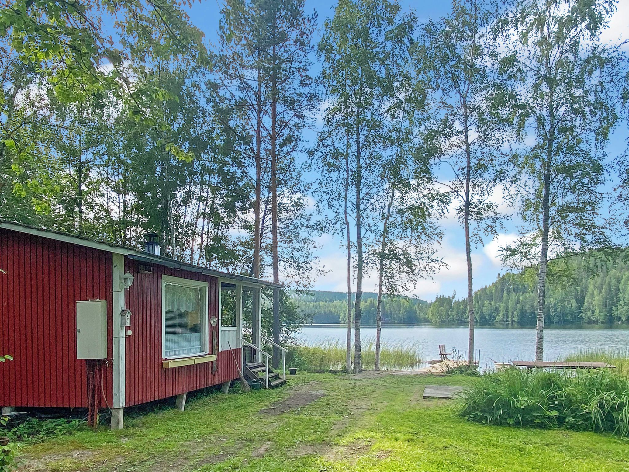 A red cabin with a dock extending into a lake, surrounded by tall trees.