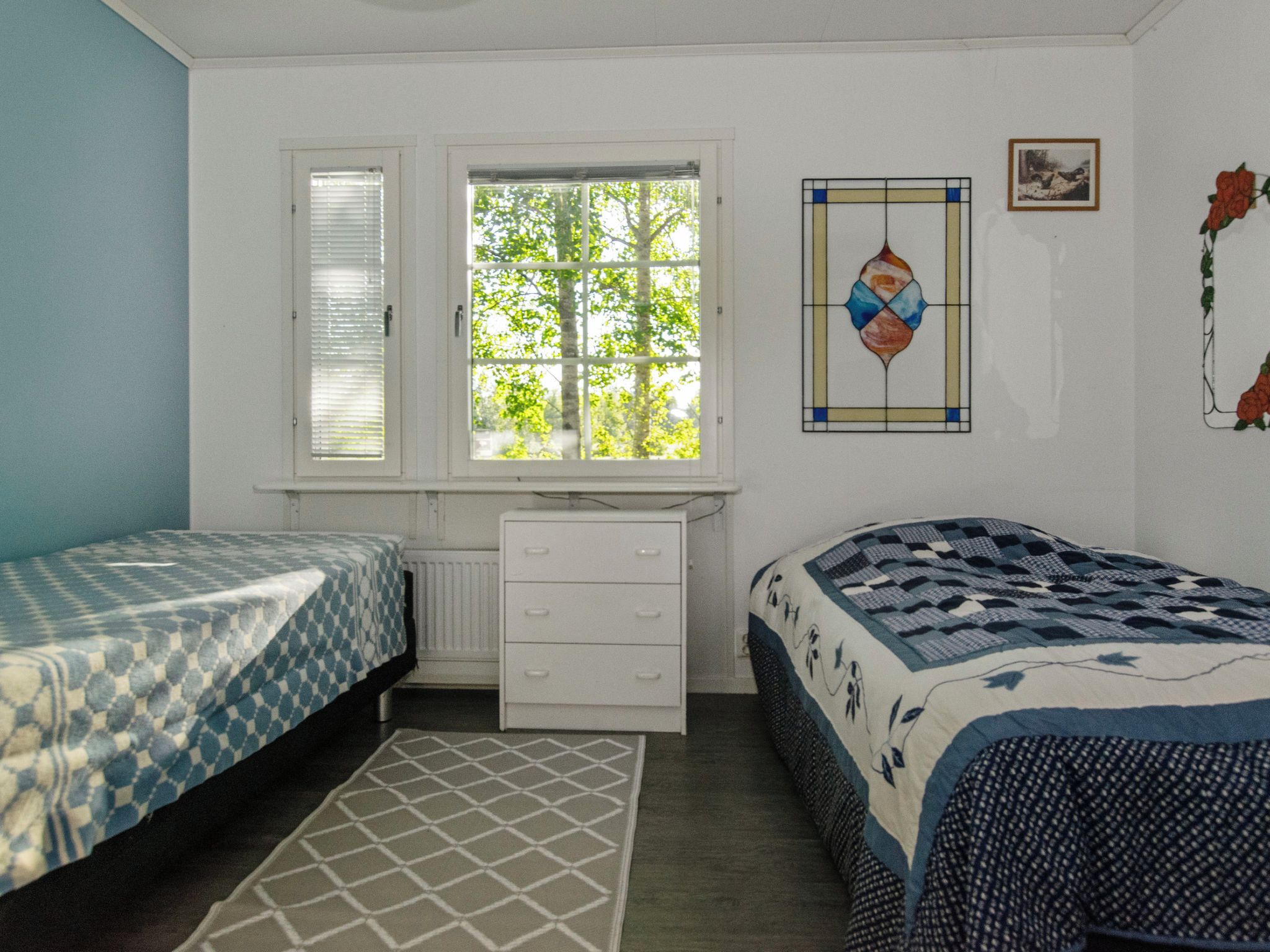 Un dormitorio con dos camas, un aparador, un radiador, una ventana con persianas y un adorno en la pared.
