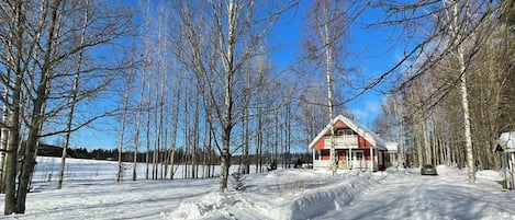 Et sneklædt landskab med et rødt hus og nøgne træer.