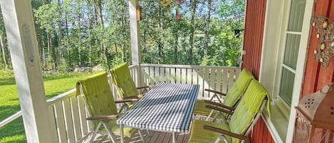 A covered outdoor area with a table and chairs, surrounded by a wooden deck and a view of a forest.