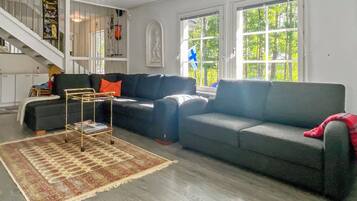 A living room with a sofa, a coffee table, and a rug. There is a staircase with a railing and a door leading to another room.