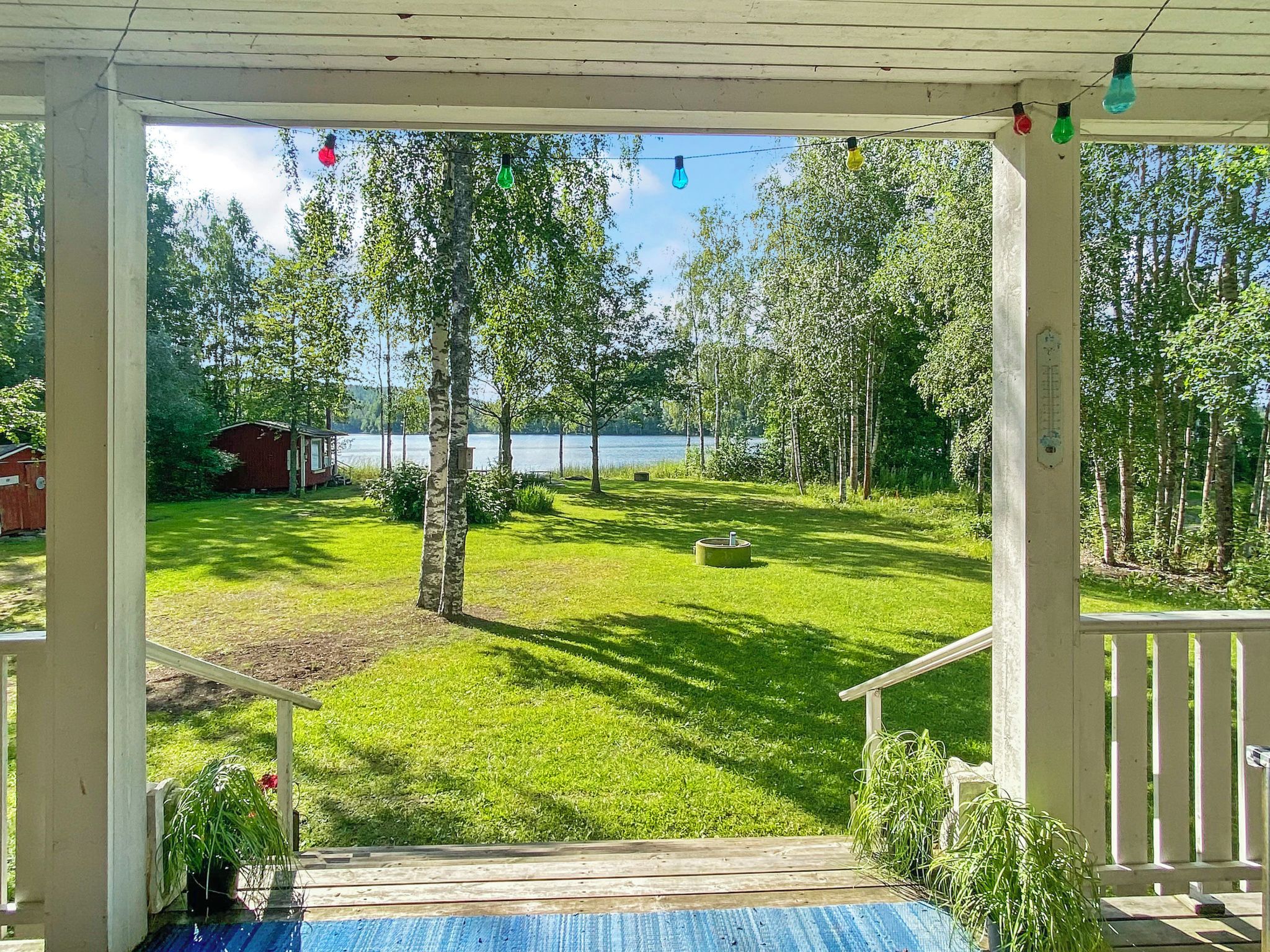 Eine überdachte Veranda mit Seeblick, ein Rasen und eine kleine Gartenhütte.