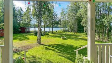 Eine überdachte Veranda mit Seeblick, ein Rasen und eine kleine Gartenhütte.