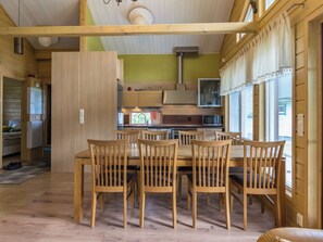 A wooden dining table with chairs, a kitchen area with a microwave, and a window with blinds. - Himosaurinko by Interhome (Kuhmoinen)