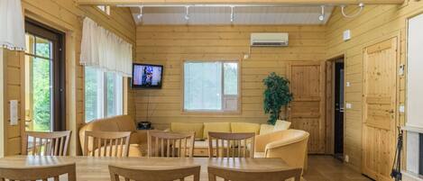 A wooden interior with a dining area, sofas, a television, and a plant.